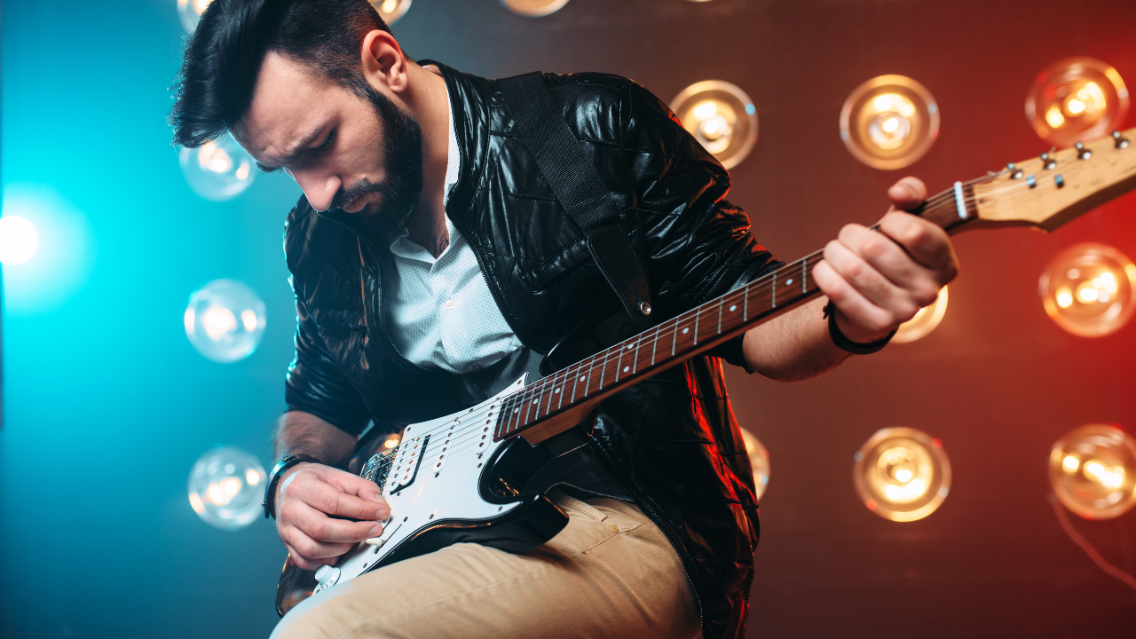man playing electric guitar on stage with lightbulbs behind him