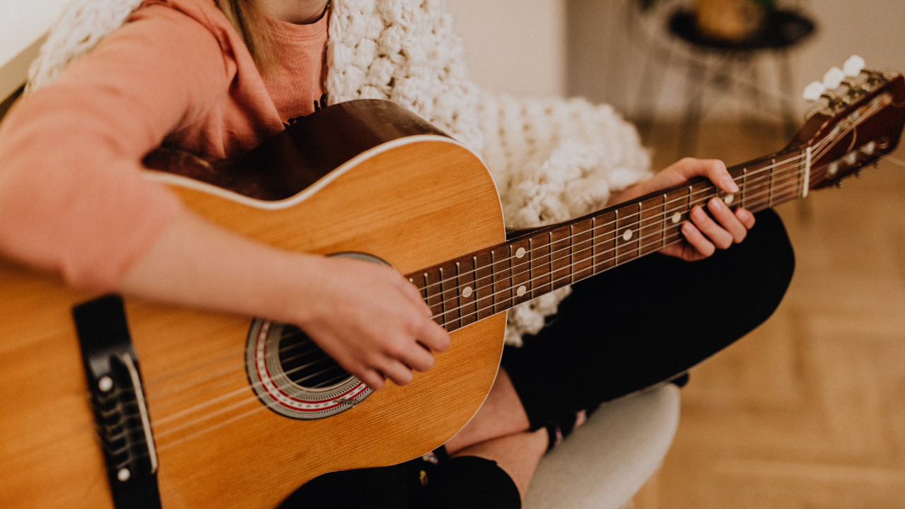 woman sitting on the floor playing an acoustic guitar