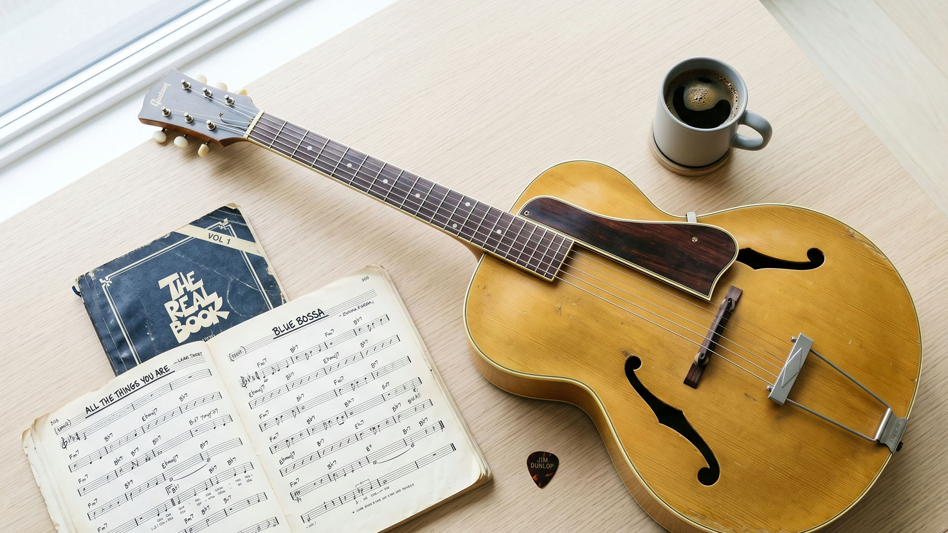 Overhead view of an archtop guitar, open fake-book, coffee, and a pick on a table