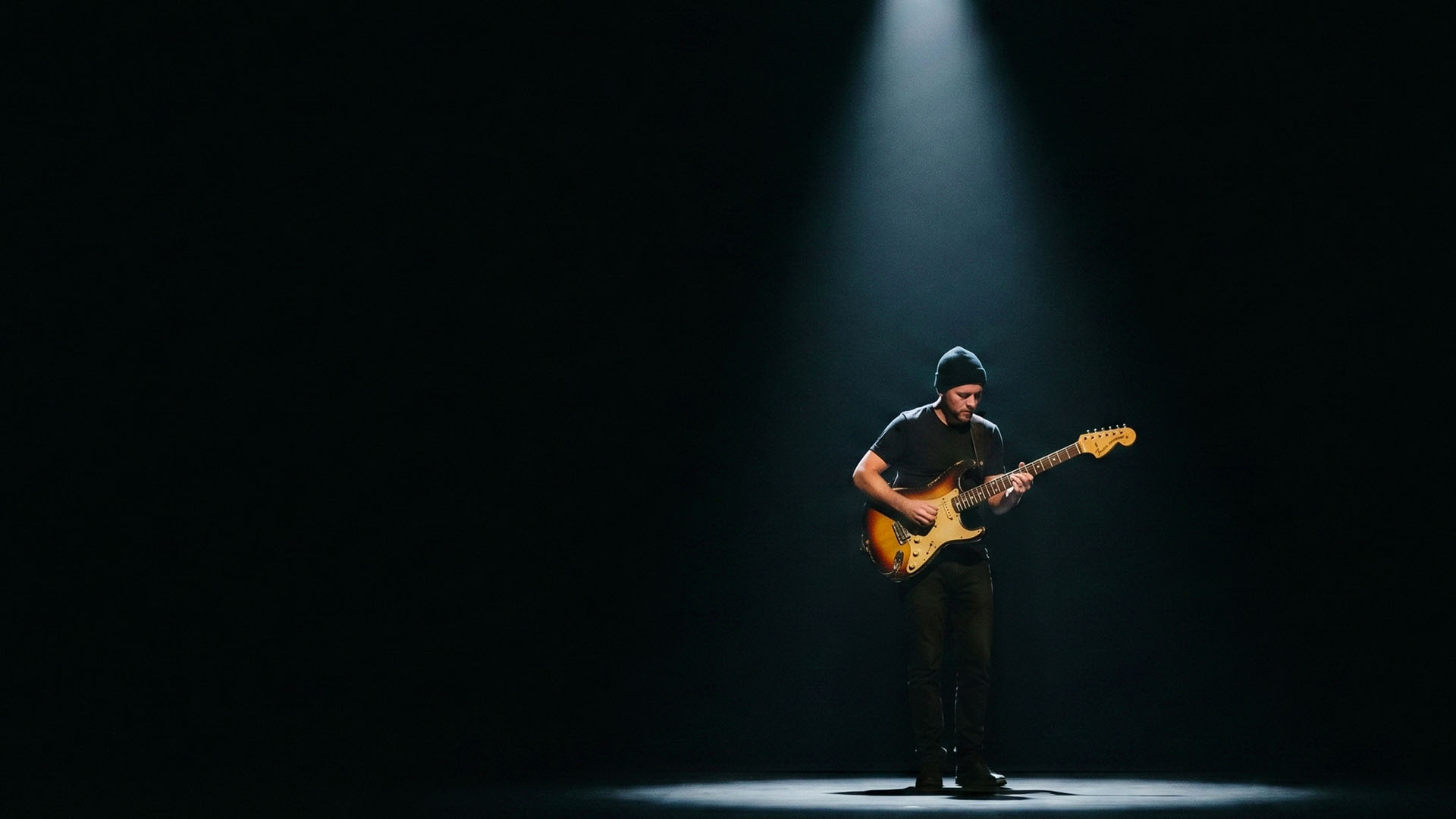Blues guitarist alone under a single spotlight, surrounded by darkness