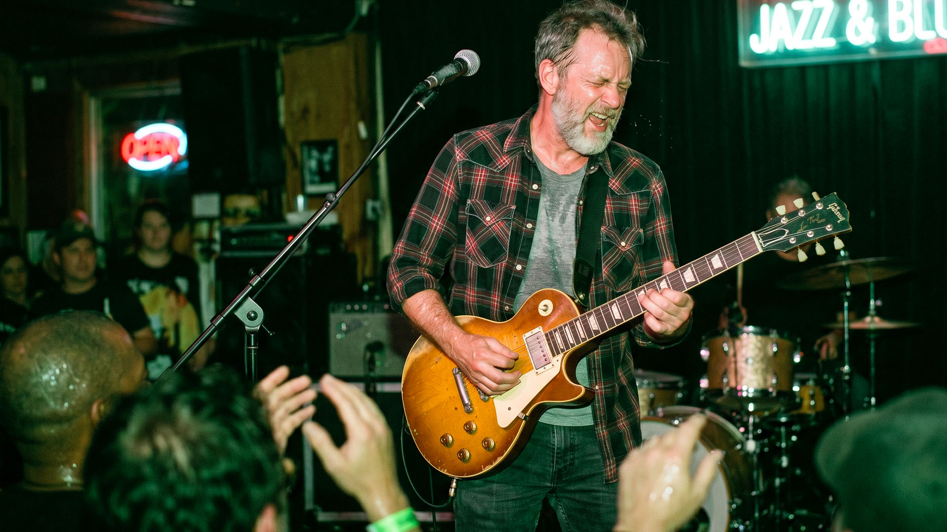 Blues guitarist mid-solo on stage, lit by harsh direct camera flash